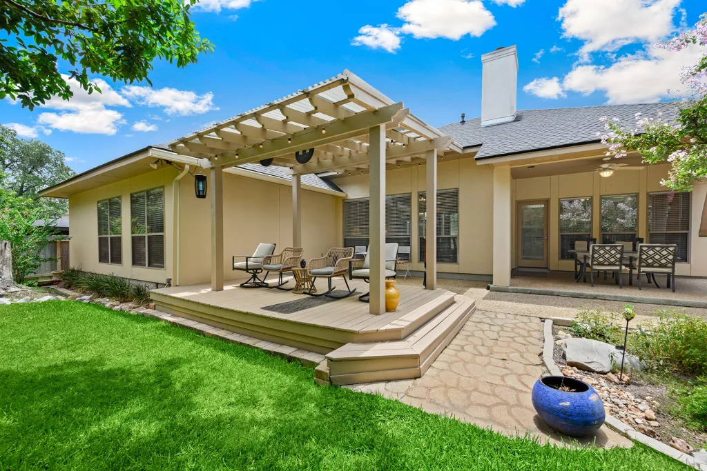 Residential backyard with a composite wood deck, light-colored pergola, comfortable patio furniture, and green lawn
