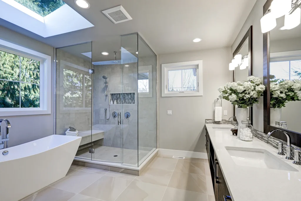Bright modern master bathroom with frameless glass shower enclosure, freestanding tub, dual vanity, and skylight
