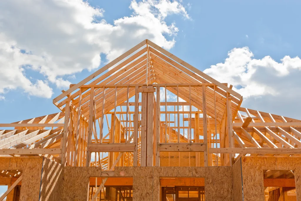 New residential house construction framing with wooden roof trusses visible against a blue, cloudy sky
